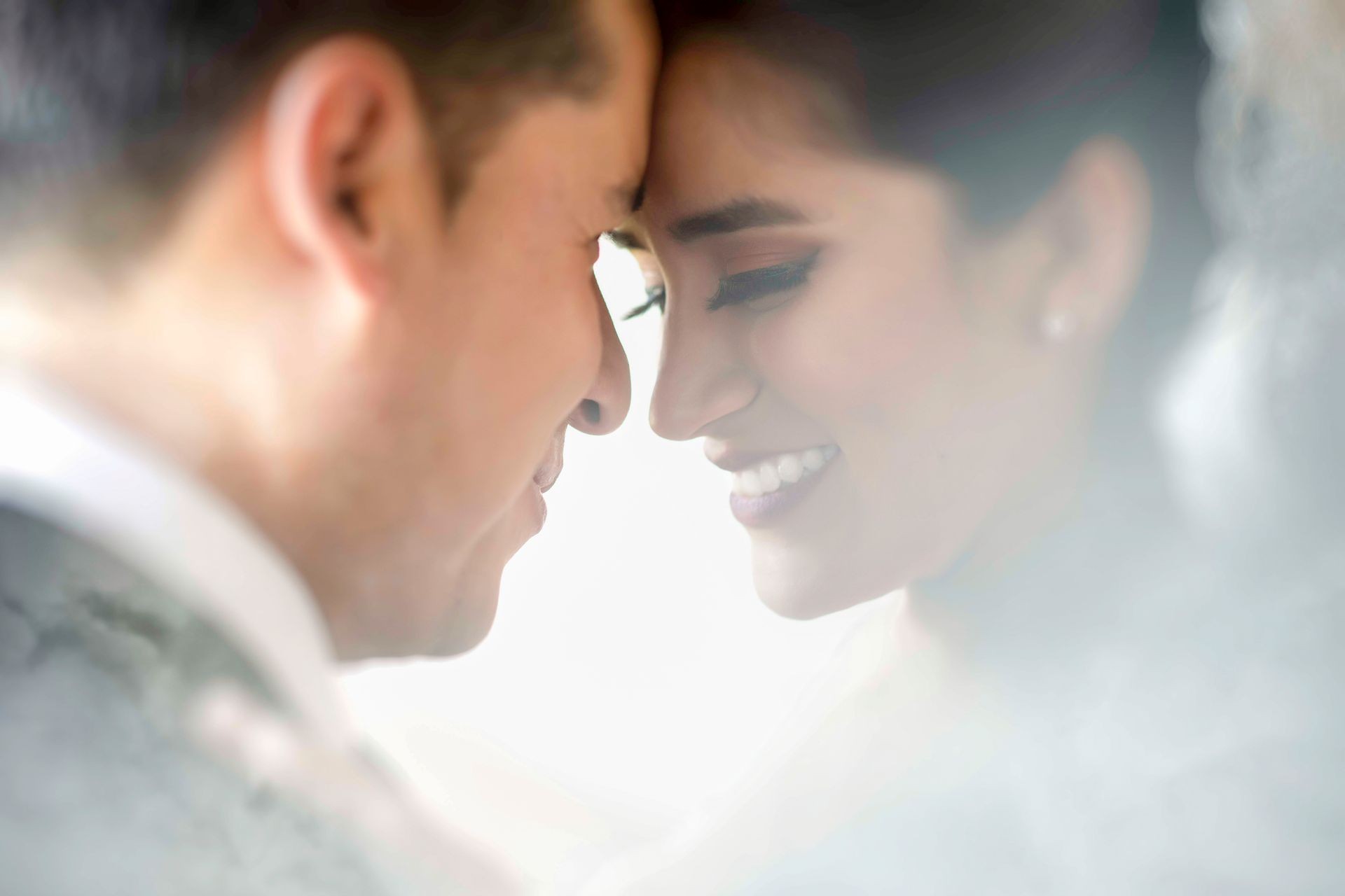Close-up of a smiling couple touching foreheads, surrounded by soft lighting and gentle focus.